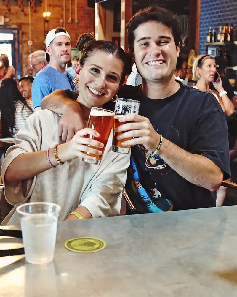 two patrons at the bar smiling and touching glasses